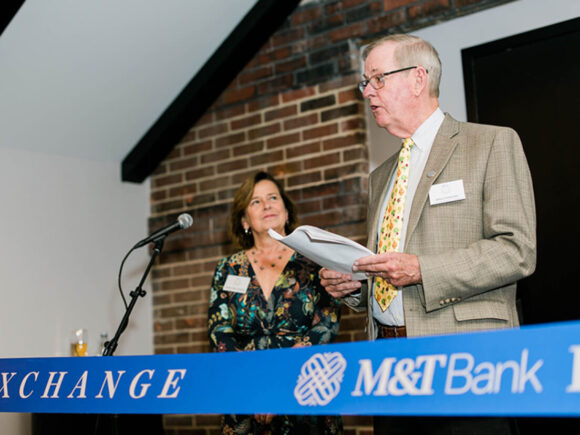 Two people stand behind a ribbon in front of a microphone. A man on the right holds papers and speaks. The ribbon displays the M&T Bank logo.